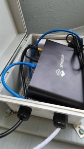 SenseCAP Helium miner inside the open outdoor enclosure with ethernet and antenna cables connected